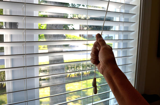 Lifestyle...This close up shot, shows an arm, lowering a bedroom window shade.